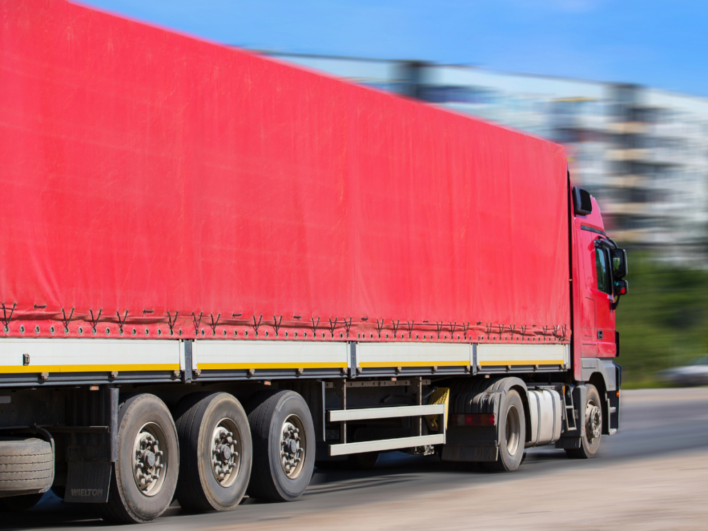Red semi-trailer truck with tautliner curtains travelling on the road