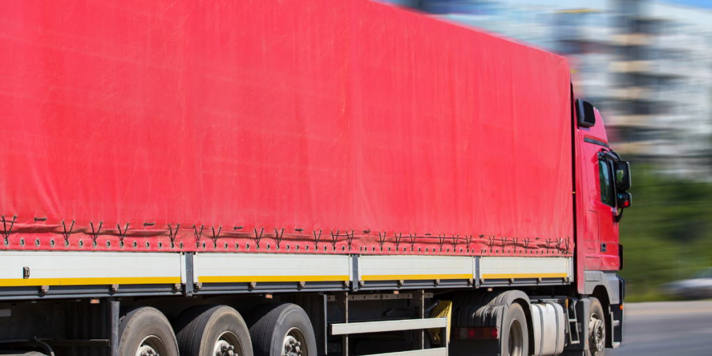 Red semi-trailer truck with tautliner curtains travelling on the road